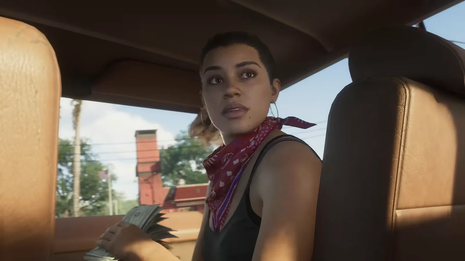 Lucia in a red bandana in a car, a fistful of cash in her hand, from Trailer 1.